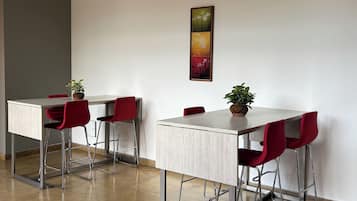 A modern dining area with a long table, red chairs, and a potted plant.