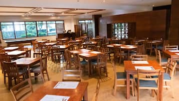 A spacious restaurant with multiple wooden tables and chairs, large windows with a view of greenery, and a modern interior design.