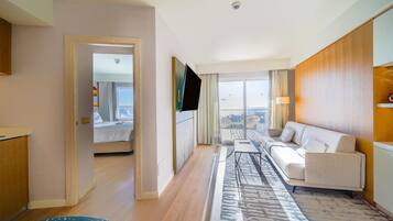 A hotel room with a sofa, a TV, a view of the outdoors, a door leading to a balcony, and a patterned rug.