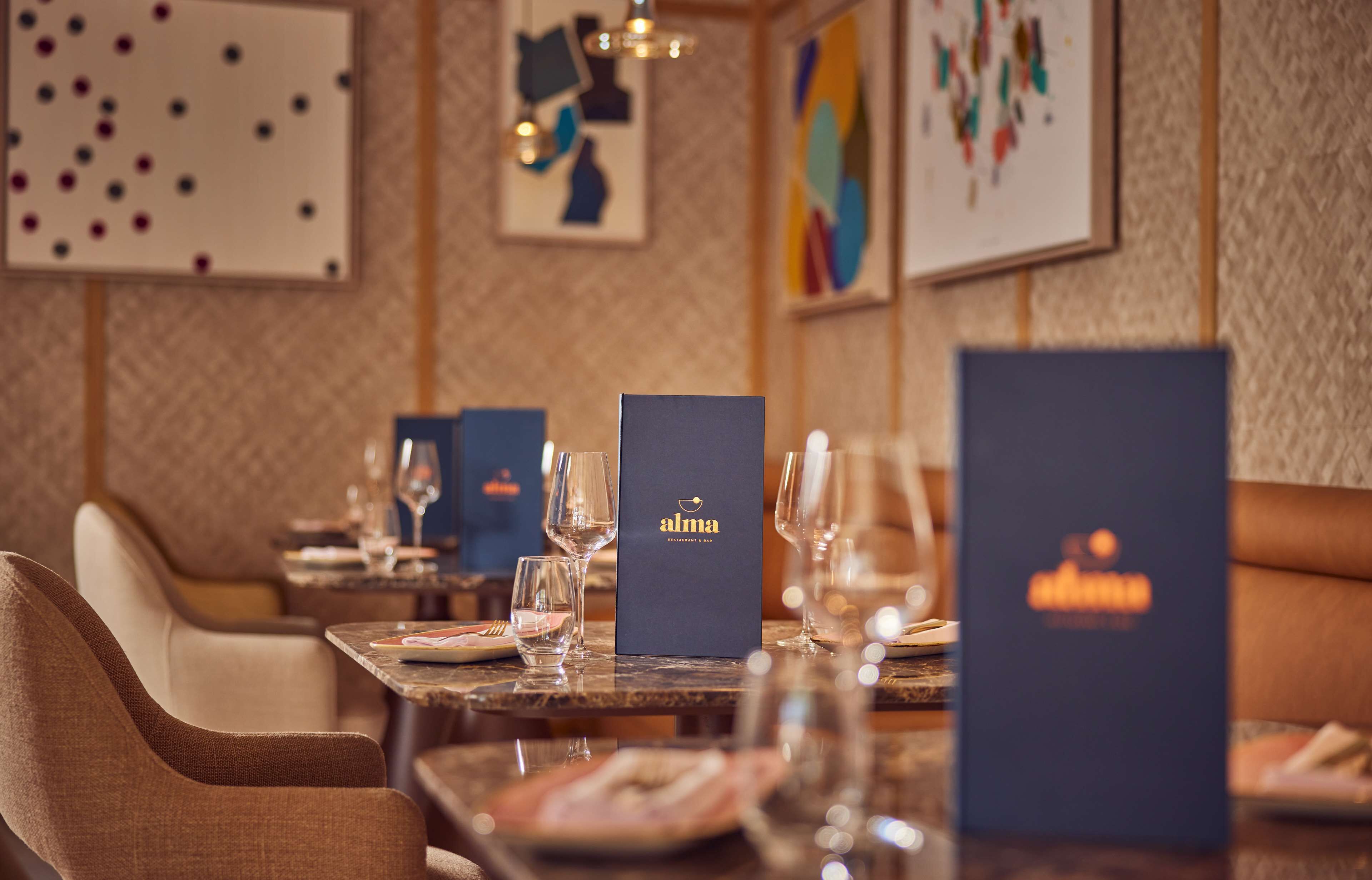 Un ambiente de restaurante con mesas preparadas para comer, destacando un atril con el menú 'alma' y una obra de arte abstracta enmarcada en la pared.