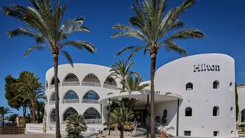 Et moderne hotel med hvid facade, flere balkoner og palmer i forgrunden.