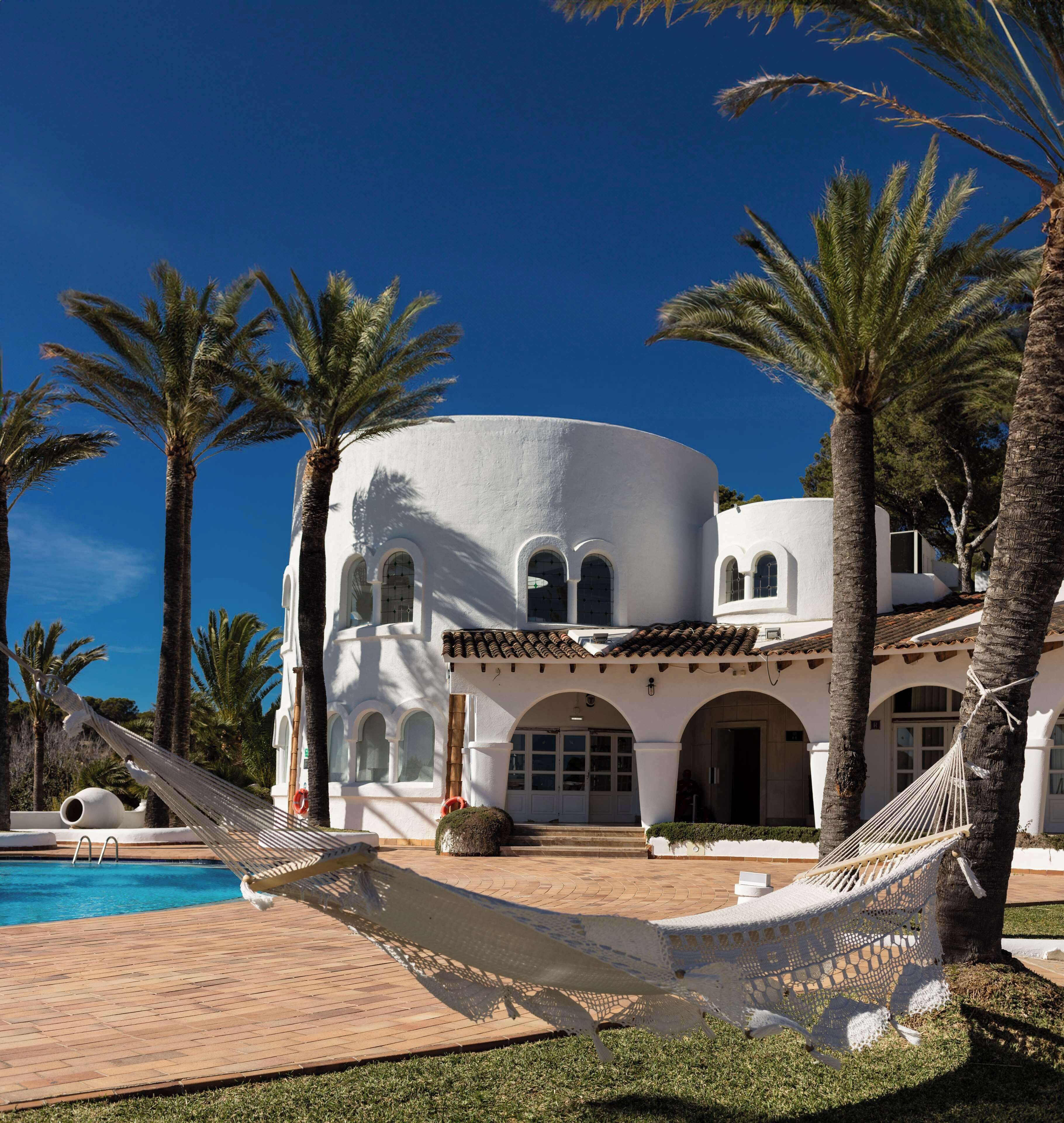 A white building with arched windows and a pool area with a hammock.