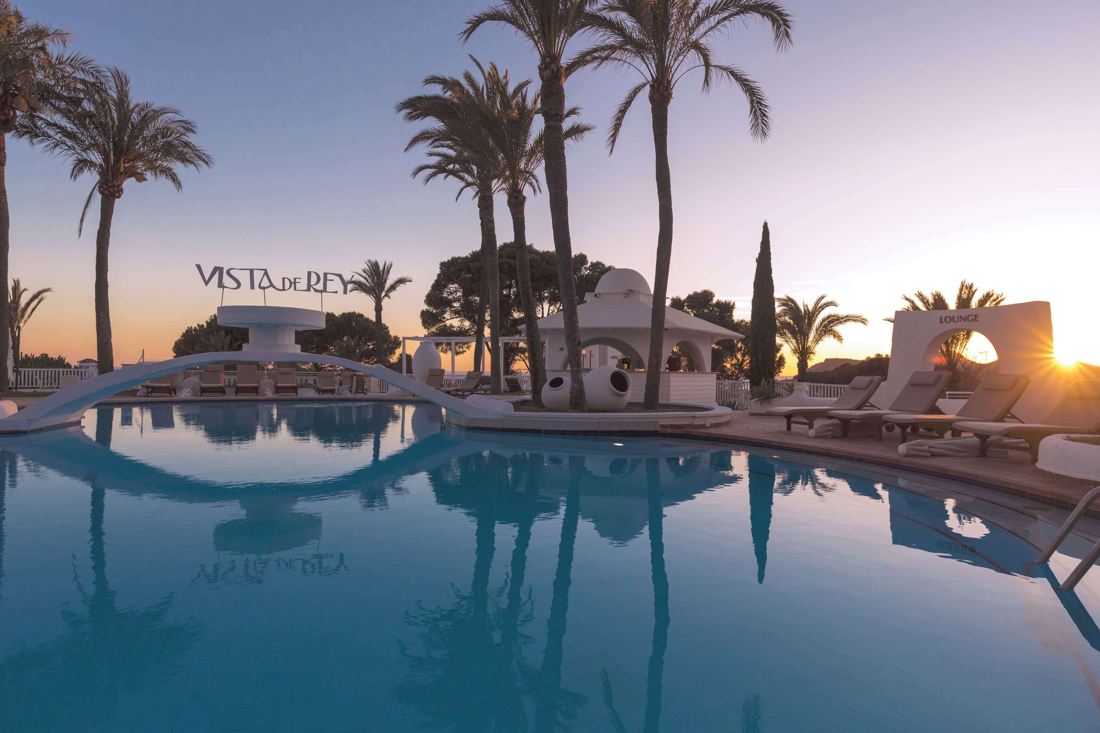 A pool area with lounge chairs, palm trees, and a building labeled "Vista de Rey."