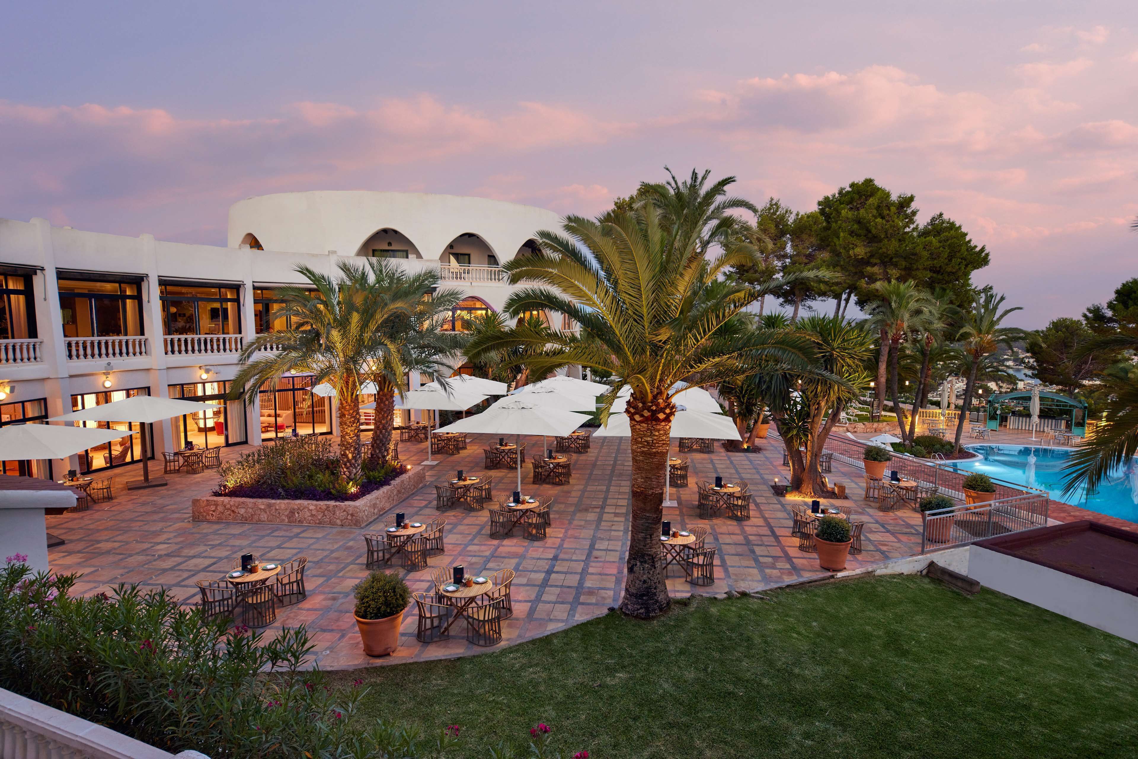 An outdoor patio area with tables and chairs, palm trees, and a pool.