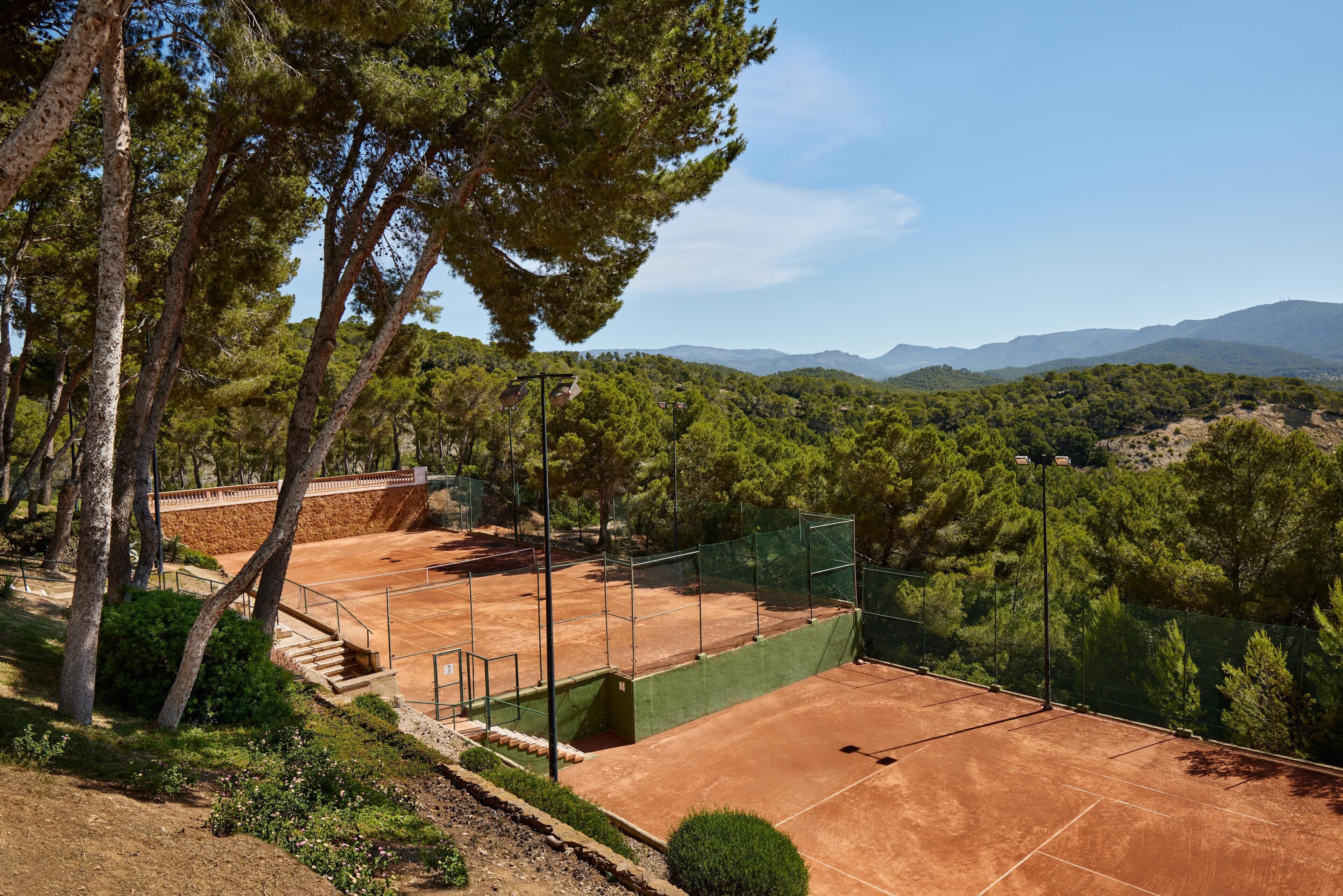 A tennis court surrounded by trees and hills.