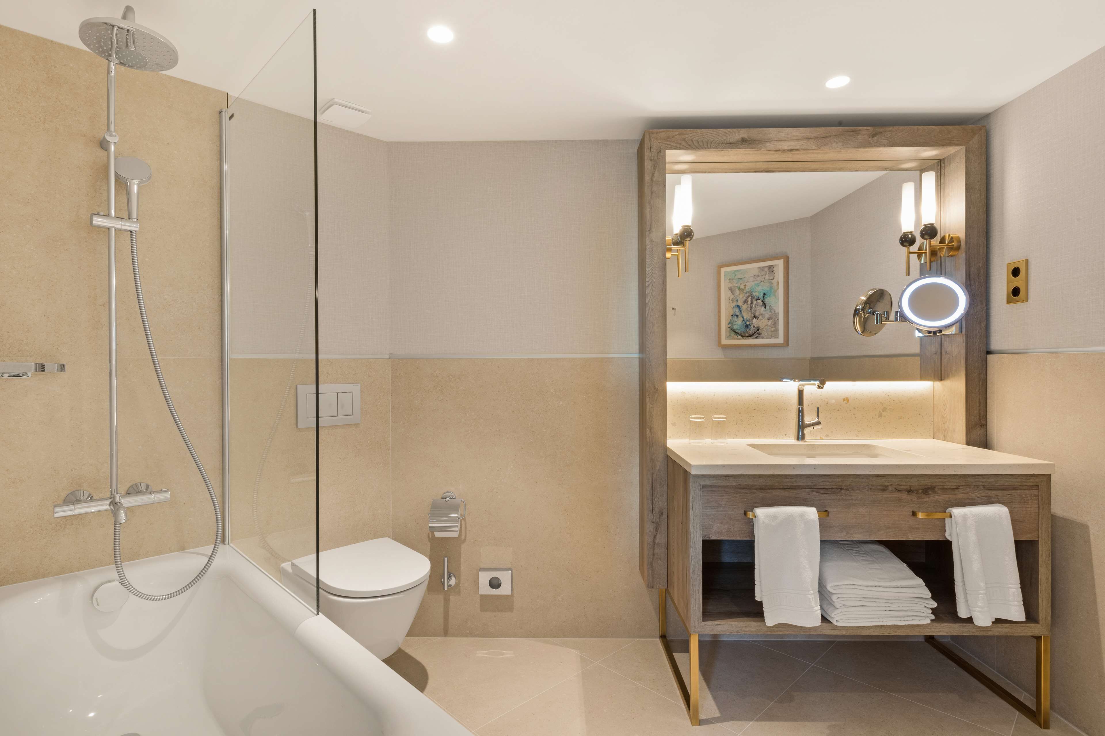 Un baño moderno con bañera, ducha, inodoro y tocador con espejo y toallero.
