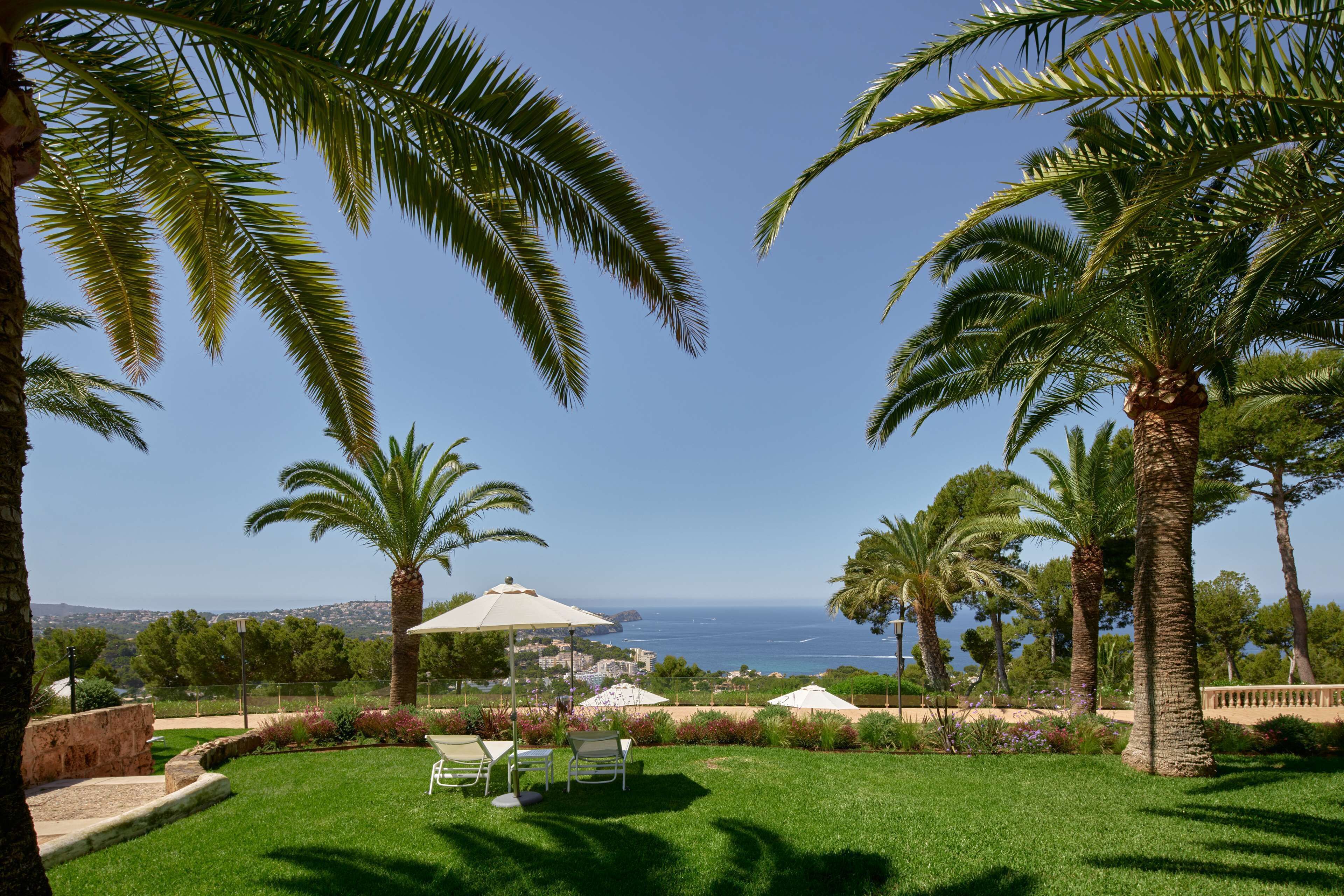 Ein gepflegter Garten mit Palmen, einer Rasenfläche und Blick aufs Meer.