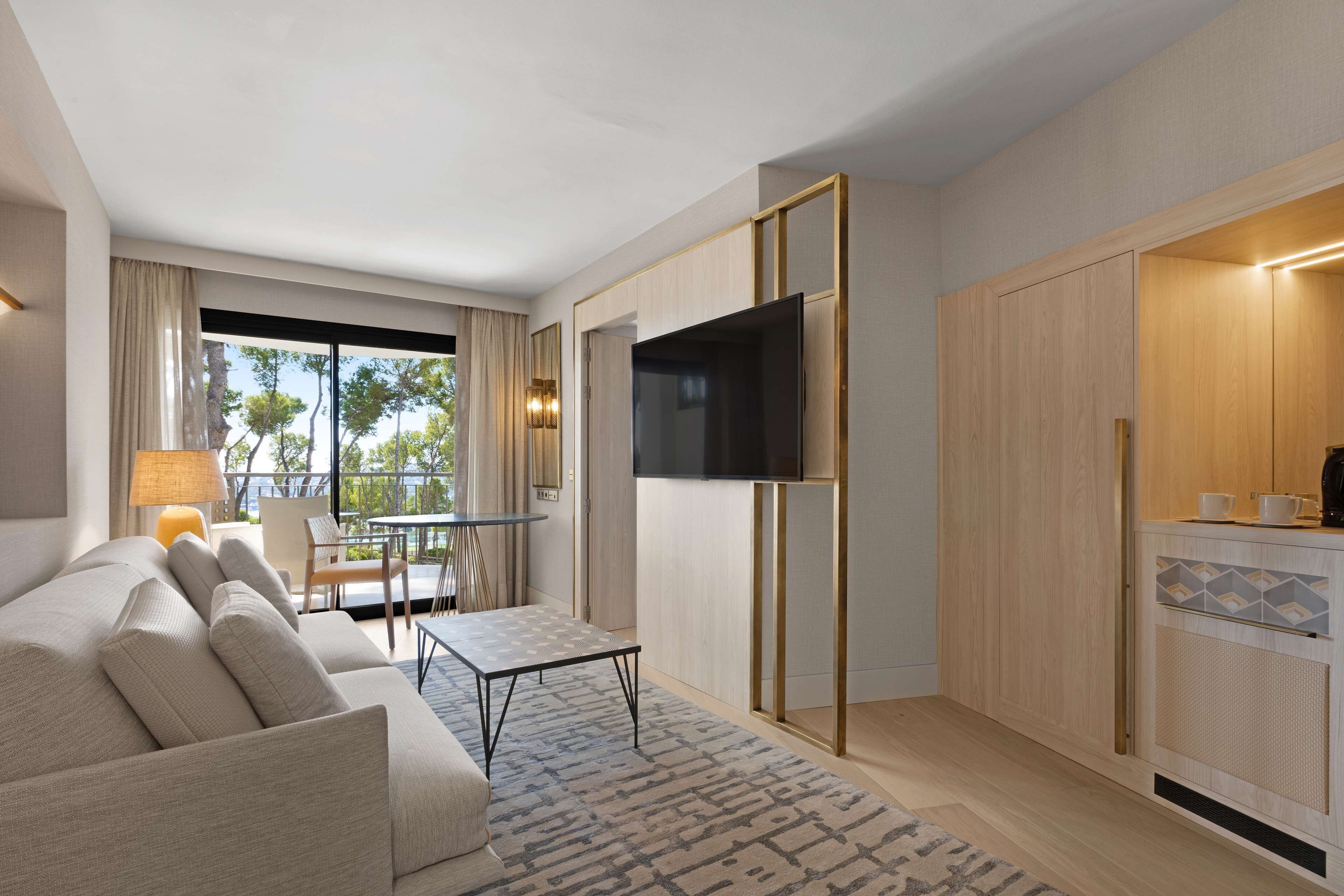 Una sala de estar moderna con un sofá, una mesa de centro y un televisor. Hay un comedor con una mesa y sillas. La habitación tiene armarios de madera y una cocina con un lavamanos y una encimera.