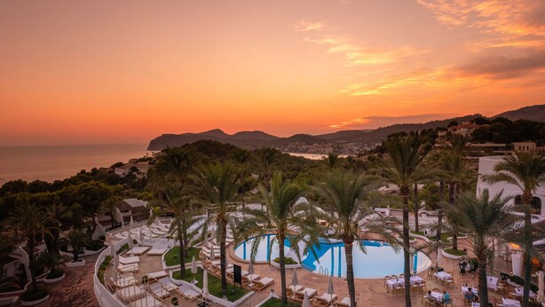 A resort with a pool, lounge chairs, and palm trees. - Hilton Mallorca Galatzo (Calvia)