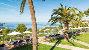 A resort with sun loungers and umbrellas, palm trees, and a view of the sea. - Hilton Mallorca Galatzo (Calvia)