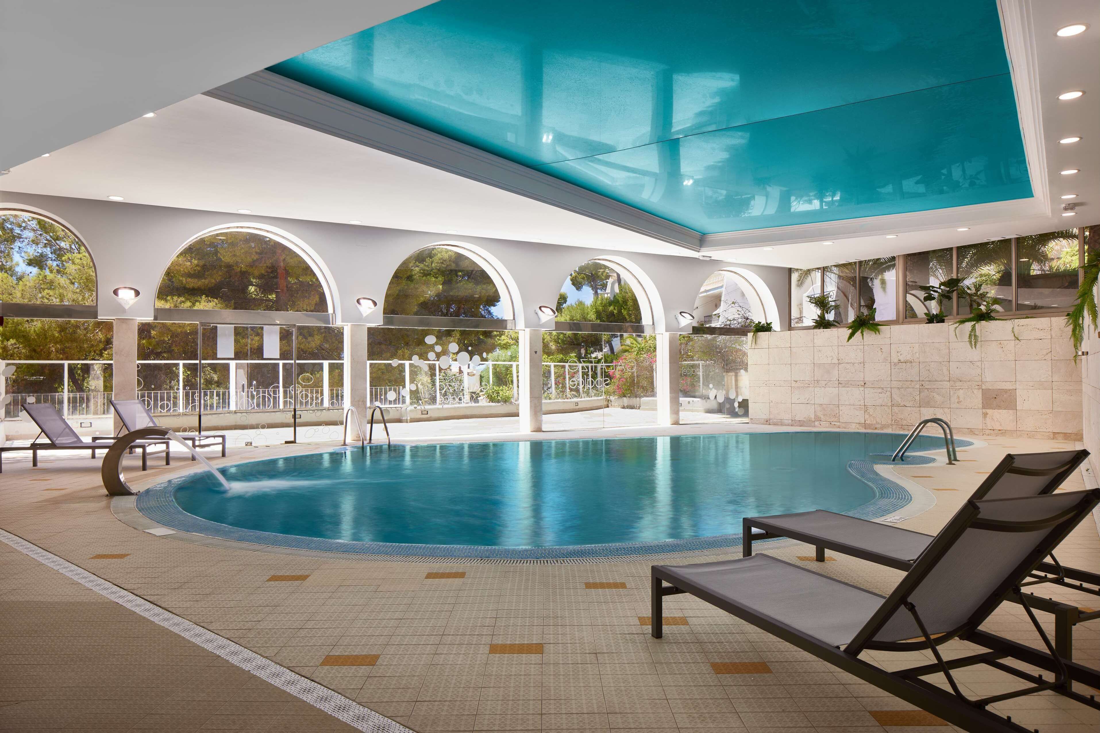 Una piscina interior con agua cristalina, rodeada de sillones de descanso y un techo de vidrio.