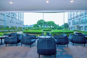 Un área de estar moderna en el interior, con vistas a un jardín ajardinado y edificios.