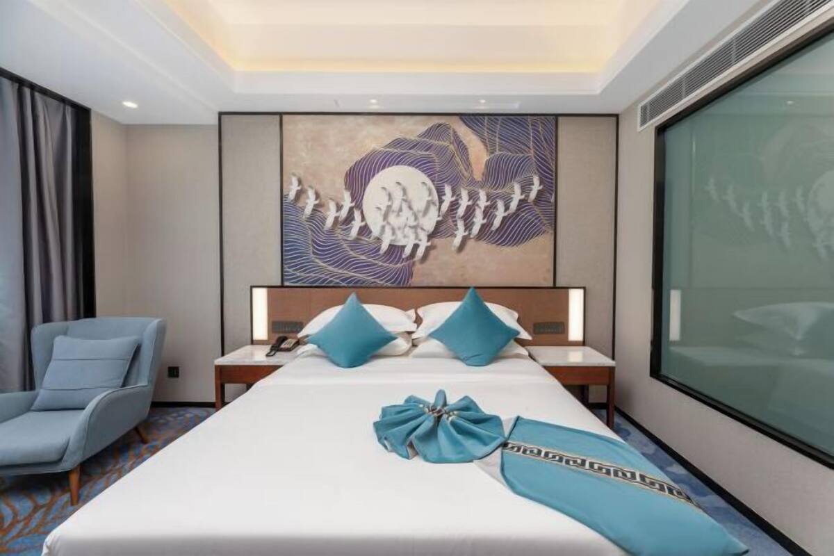 A hotel room with a large bed, a nightstand, a chair, and a wall art piece.