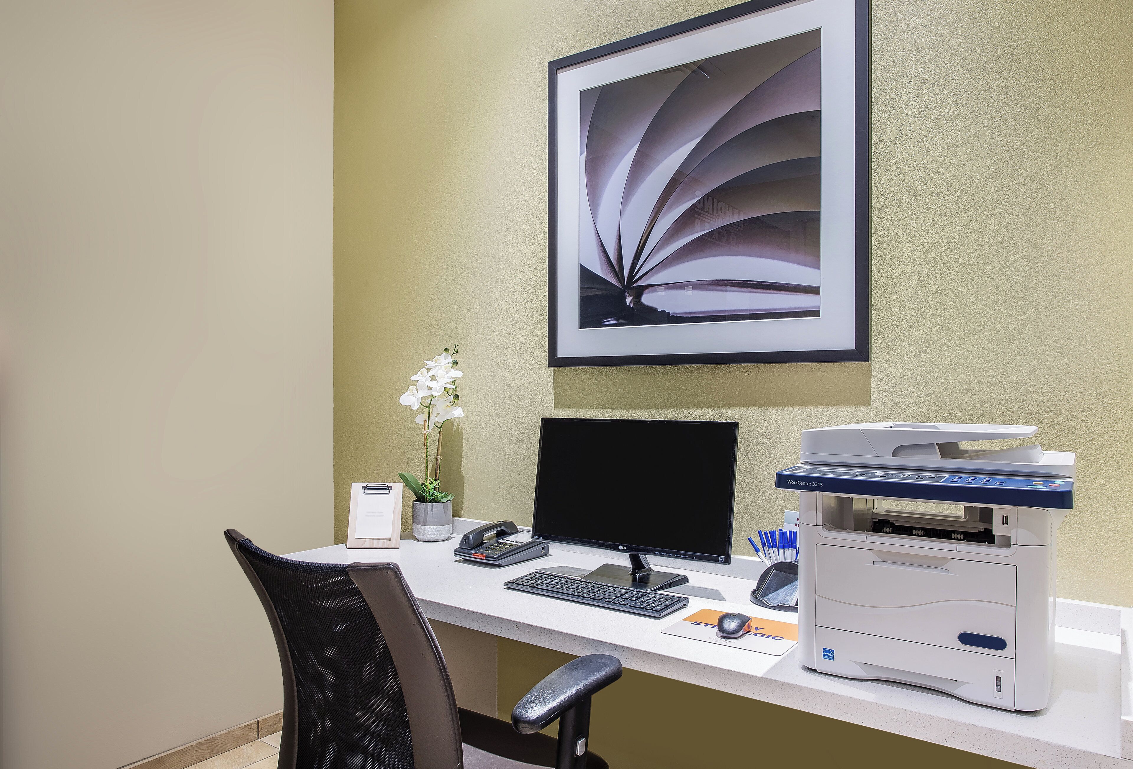 A modern office desk with a computer, printer, and a framed abstract art piece on the wall.