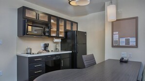 A modern kitchen with dark cabinetry, a microwave, refrigerator, and a dining table with a chair. - Candlewood Suites Bowling Green by IHG (Bowling Green)