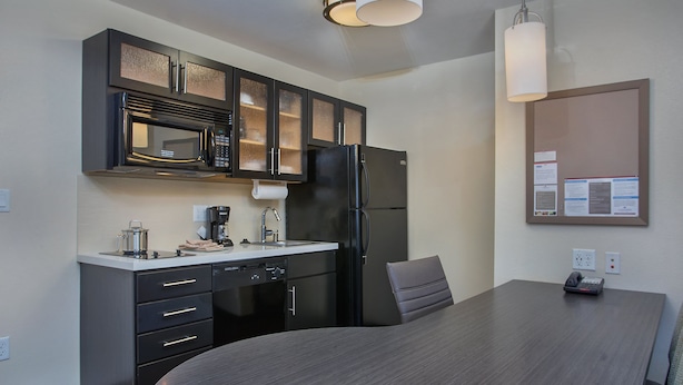 Une cuisine moderne avec des meubles de couleur sombre, un four à micro-ondes, un réfrigérateur et une table à manger avec une chaise.