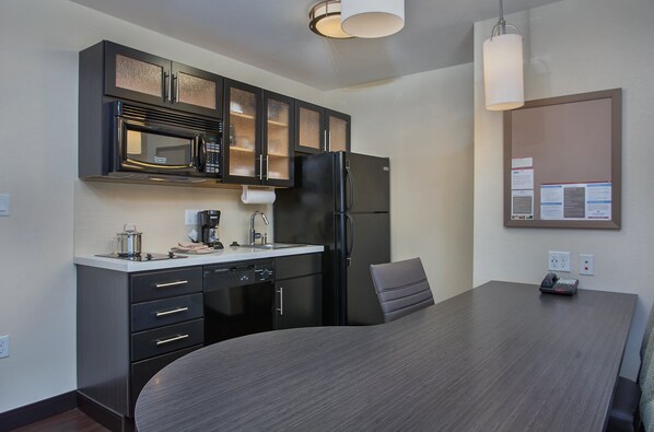 Una cocina moderna con armarios oscuros, un microondas, un refrigerador y una mesa de comedor con una silla.
