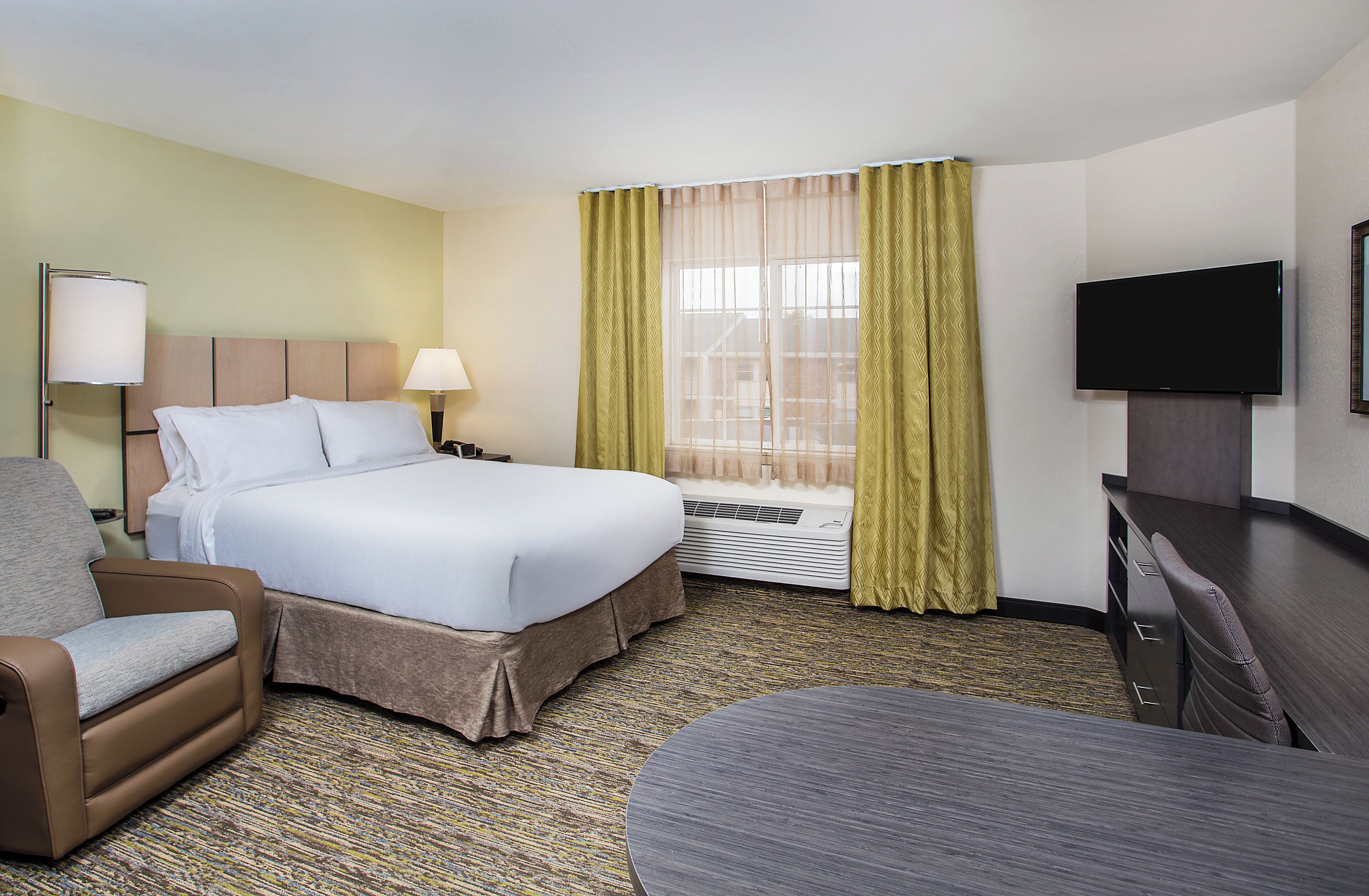 A hotel room with a bed, a desk, a chair, a television, and a window with curtains.