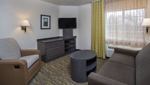 A hotel room with a sofa, a TV, a small table, and a window with curtains. - Candlewood Suites Bowling Green by IHG (Bowling Green)