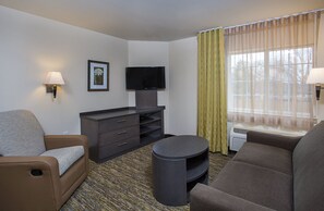 A hotel room with a sofa, a TV, a small table, and a window with curtains.