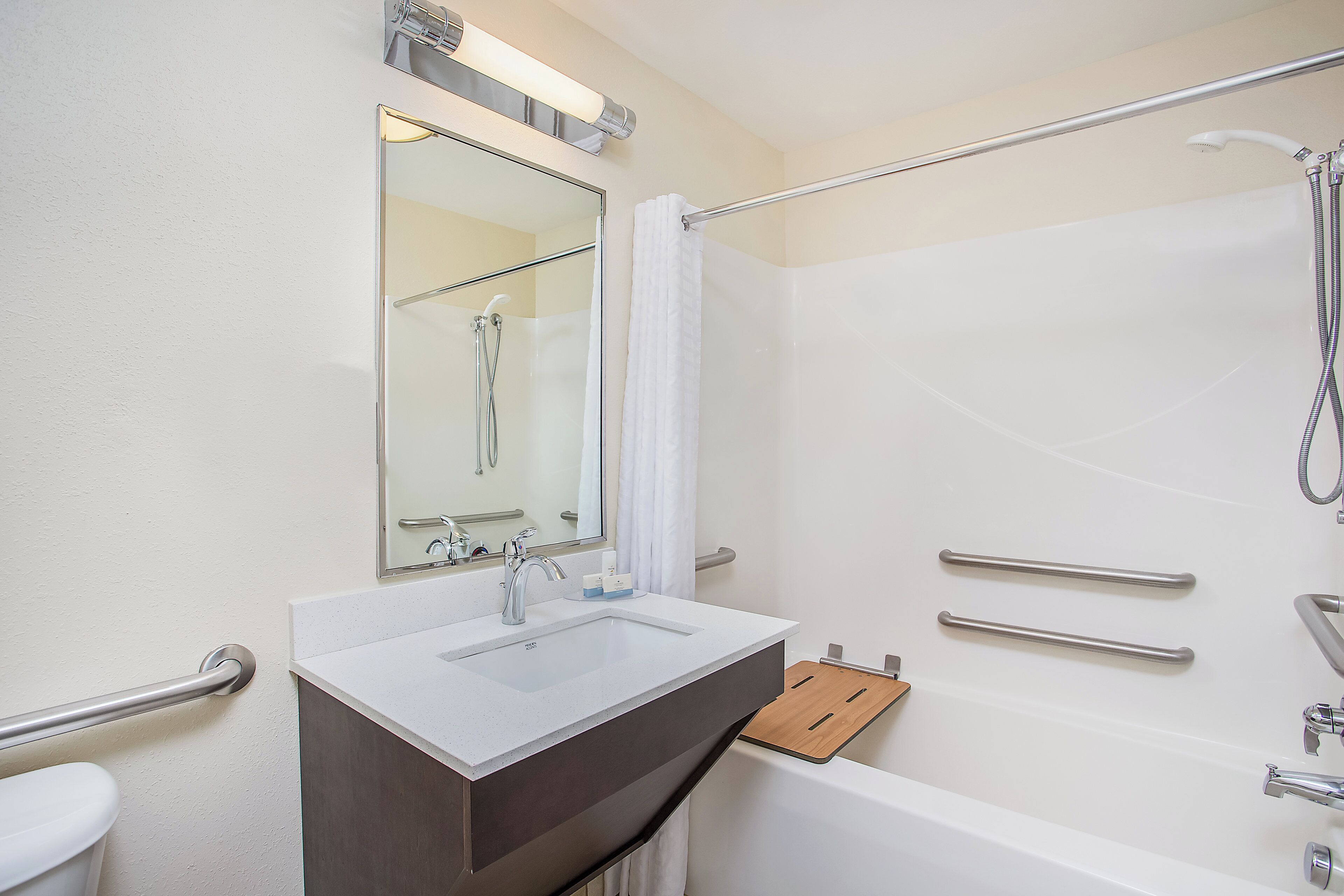A bathroom with a white sink, a mirror, a shower with a handheld showerhead, and a grab bar.