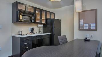 A modern kitchen with a microwave, refrigerator, and a dining table with a chair.