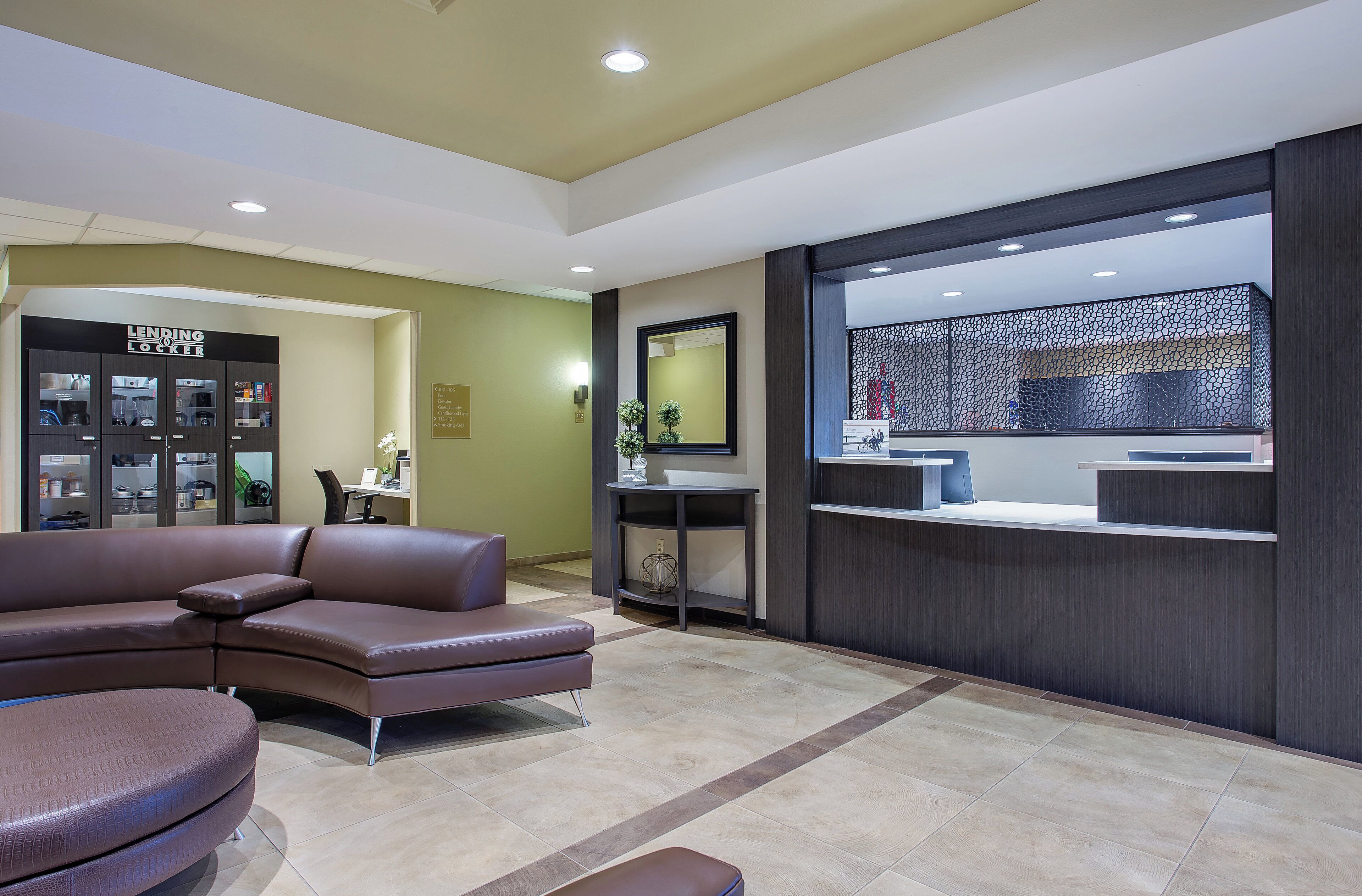 A modern hotel lobby with a sectional sofa, a reception desk, and a wall-mounted mirror.