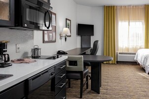 Habitación de hotel con kitchenette, televisor de pantalla plana, escritorio con silla y cama.