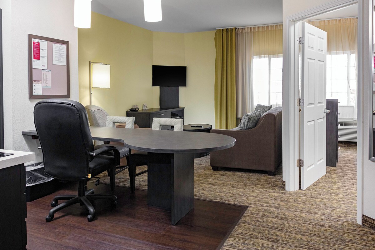 A hotel room with a dining table, a sofa, a TV, and a door leading to another room.