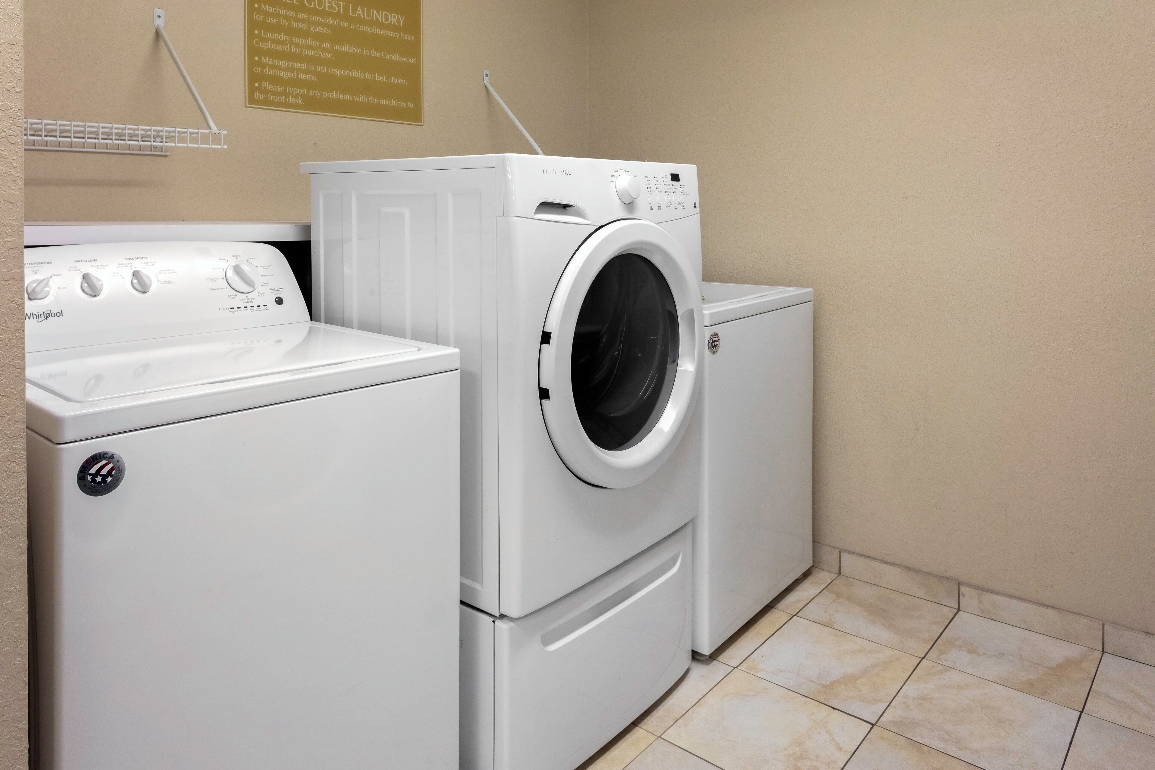A laundry area with a front-loading washer and dryer, a wall-mounted shelf, and a sign detailing laundry policies.