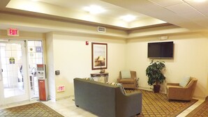 A lobby with a reception desk, two armchairs, a sofa, a TV mounted on the wall, and an exit sign.