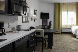 A hotel room with a kitchenette, a desk, a chair, a bed, a TV, and a window with curtains. - Candlewood Suites Warner Robins/Robins AFB by IHG (Warner Robins)