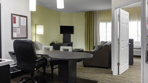 A hotel room with a conference table, two chairs, a sofa, a TV, and a door leading to another room.