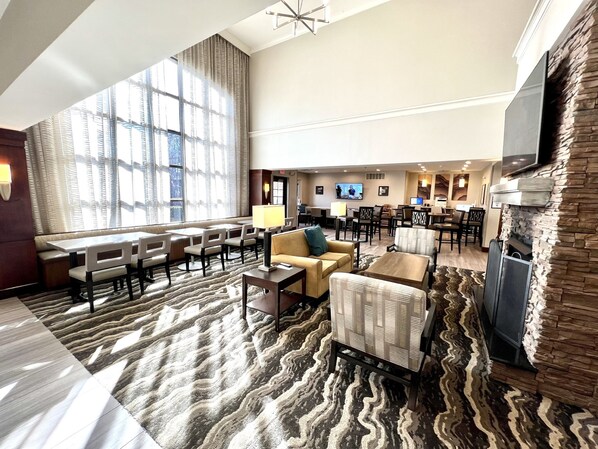A spacious lobby with a large seating area, a flat-screen TV mounted on the wall, and a stone accent wall. - Staybridge Suites Detroit Novi by IHG (Novi)