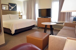 Una habitación de hotel con una cama grande, televisión, una mesita y un sofá.