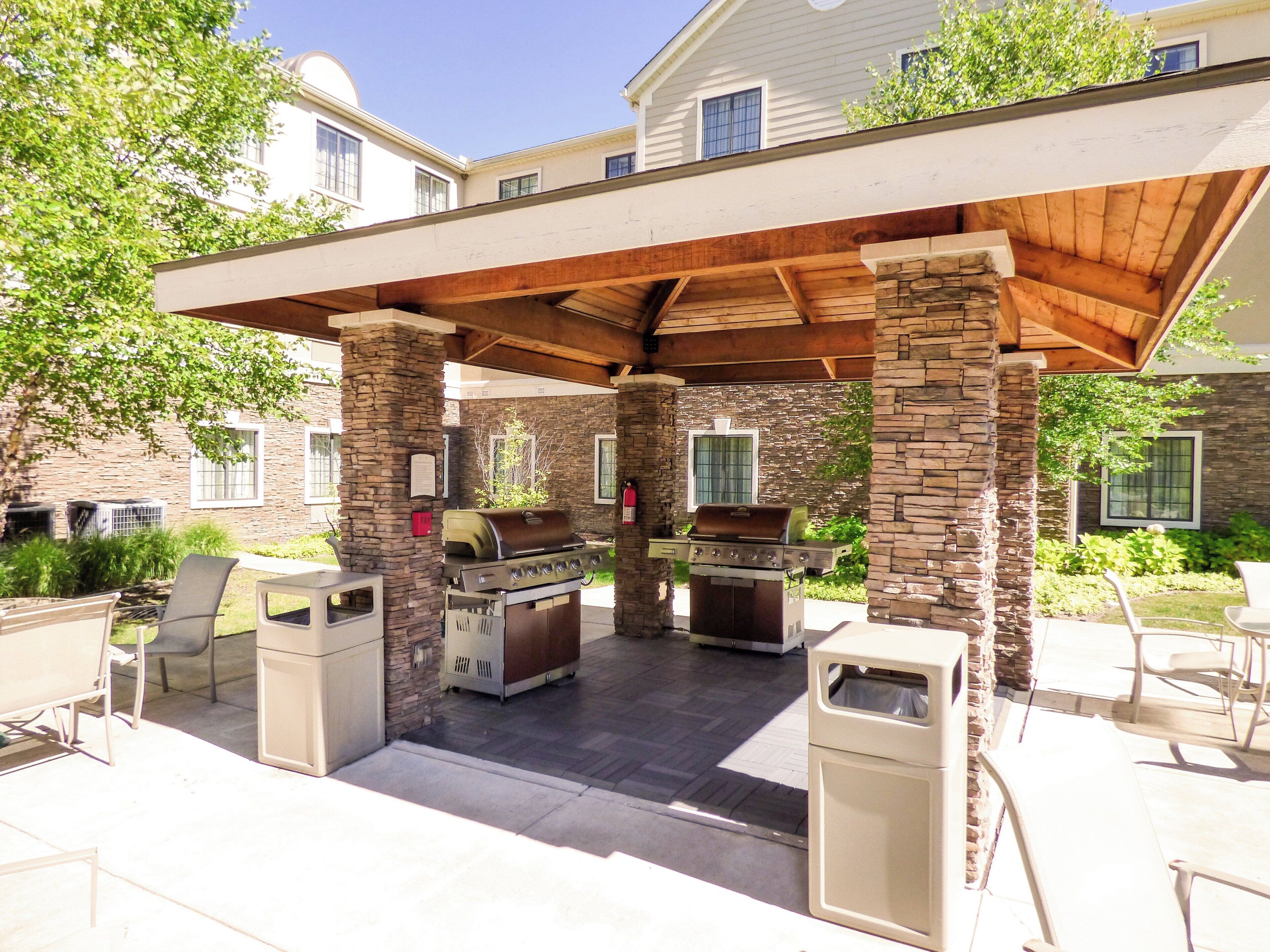 An outdoor patio with a stone and wood barbecue area, seating, and a covered section.