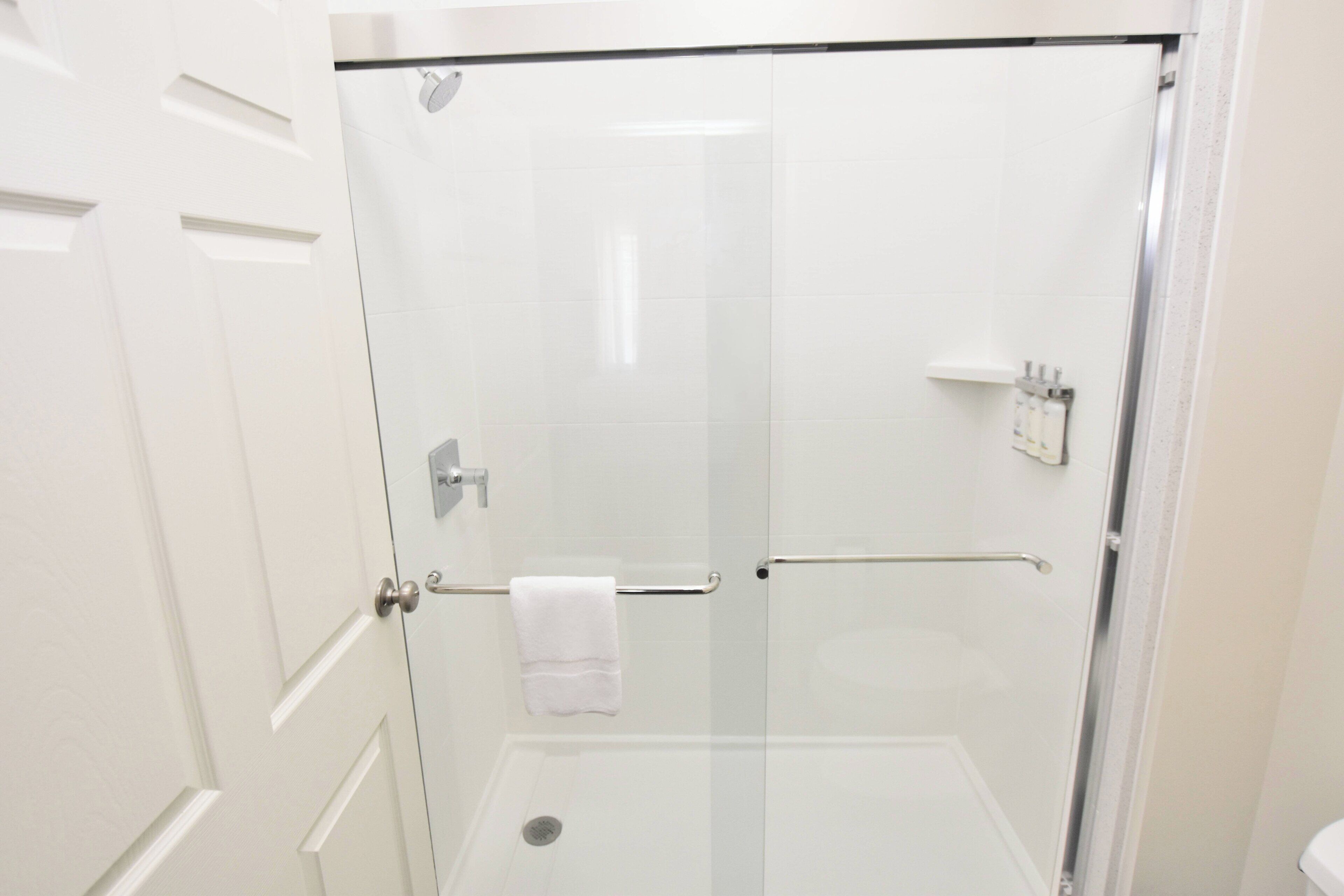 A glass-enclosed shower with a white towel hanging on a metal bar, a glass door, and a white tiled wall.