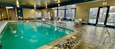 An indoor swimming pool with tiled flooring and a view of the outside through large windows.