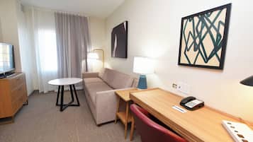 A hotel room with a sofa, a desk with a phone, a lamp, and a TV.