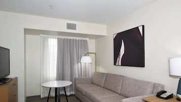 A hotel room with a sofa, a small round table, a television, a lamp, and a painting on the wall.