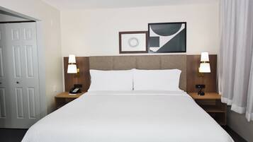 Ein Hotelzimmer mit einem großen Bett, zwei Nachttischen mit Lampen, einer Tür und zwei gerahmten Bildern an der Wand.