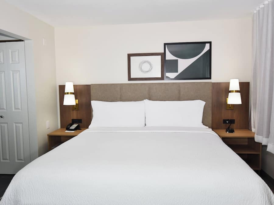 Ein Hotelzimmer mit einem großen Bett, zwei Nachttischen mit Lampen, einer Tür und zwei gerahmten Bildern an der Wand.