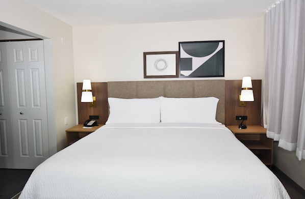 A hotel room with a large bed, two bedside tables with lamps, a door, and two framed pictures on the wall.
