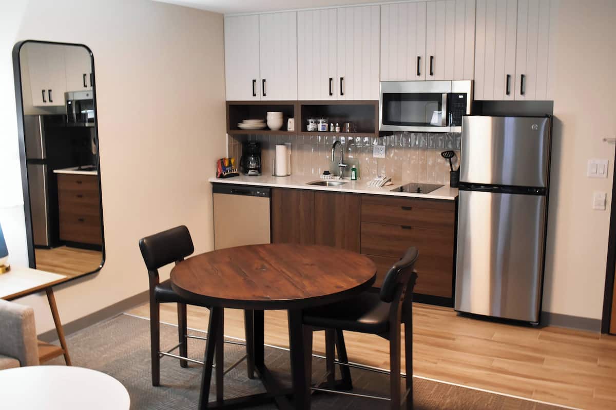 A modern kitchen with wooden cabinets, a stainless steel refrigerator, and a round dining table with chairs.