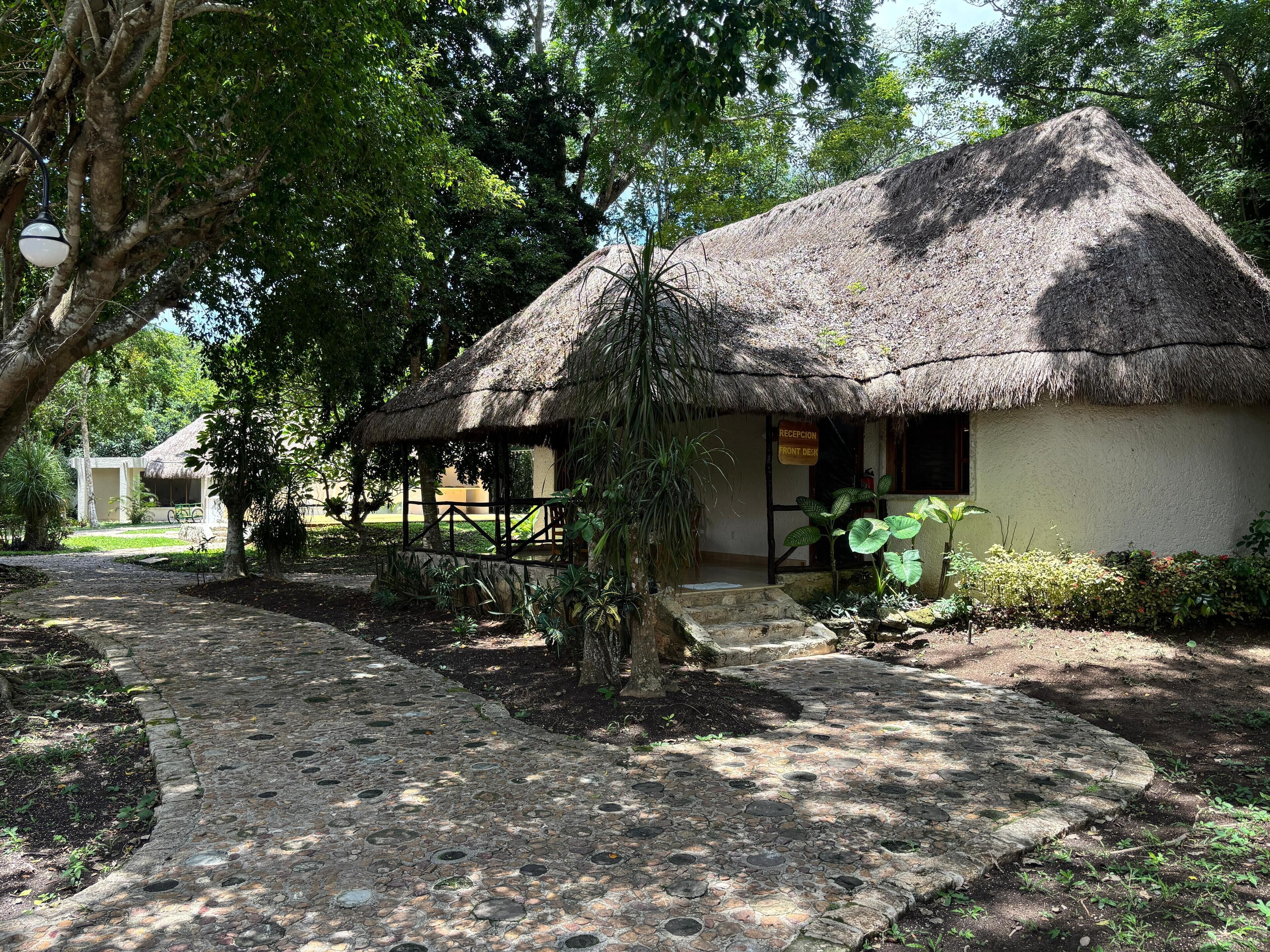 A thatched-roof hut with a reception desk labeled "RECEPTION FRONT DESK."