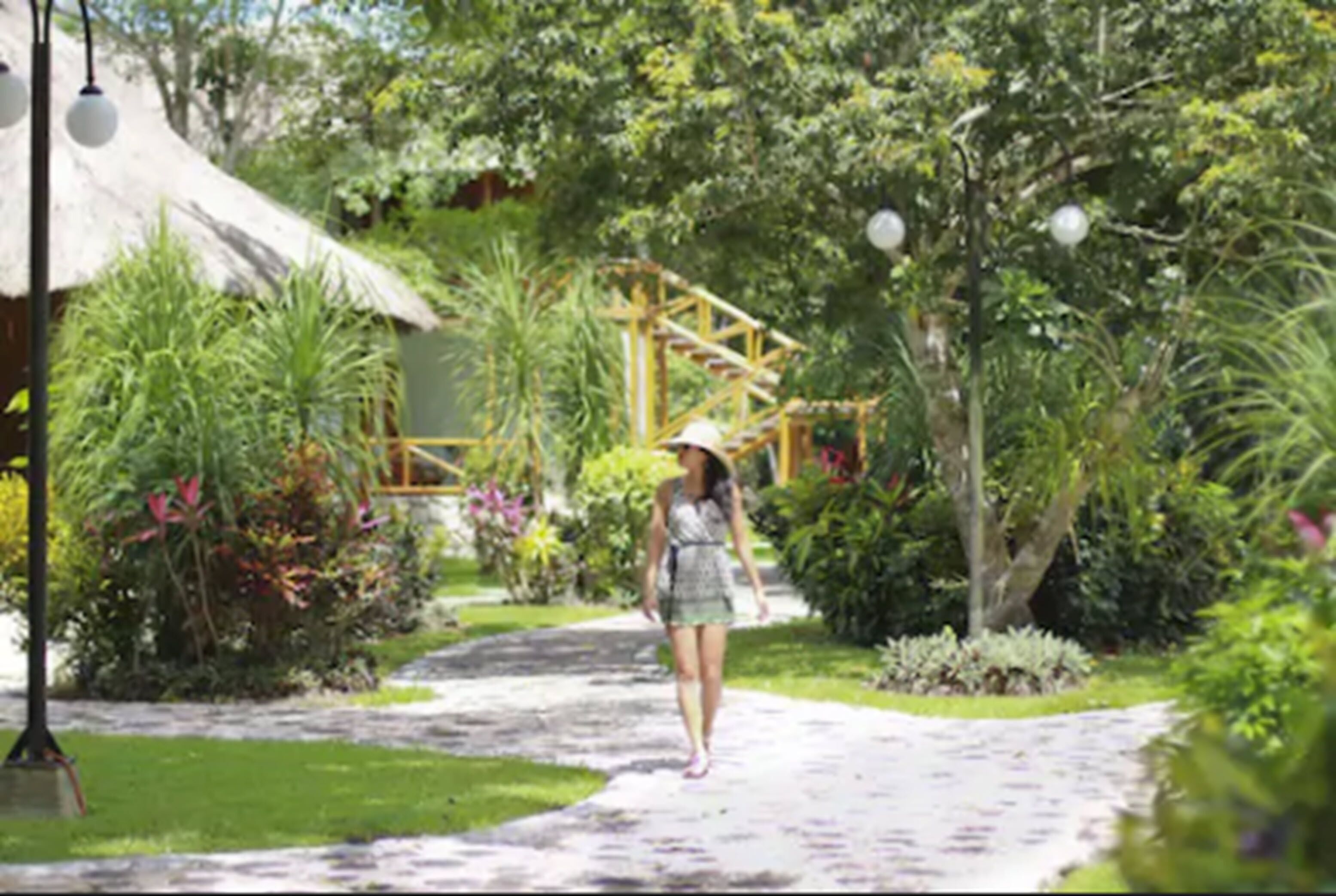 A pathway in a lush garden with a thatched-roof structure and a wooden pergola.