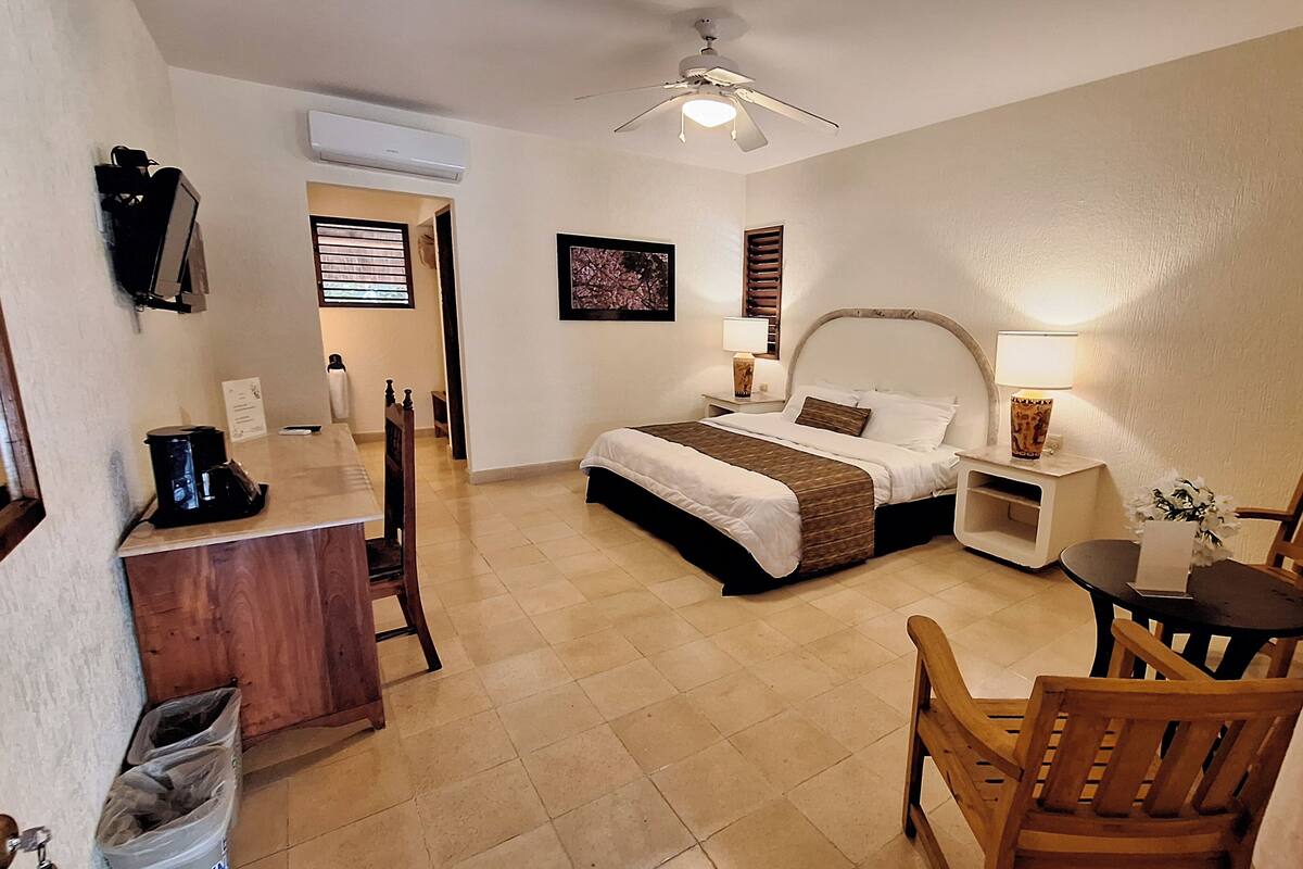 A hotel room with a bed, bedside tables, a desk, a chair, and a ceiling fan.