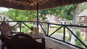 Una terraza de madera con techo de paja, una mesa y sillas.