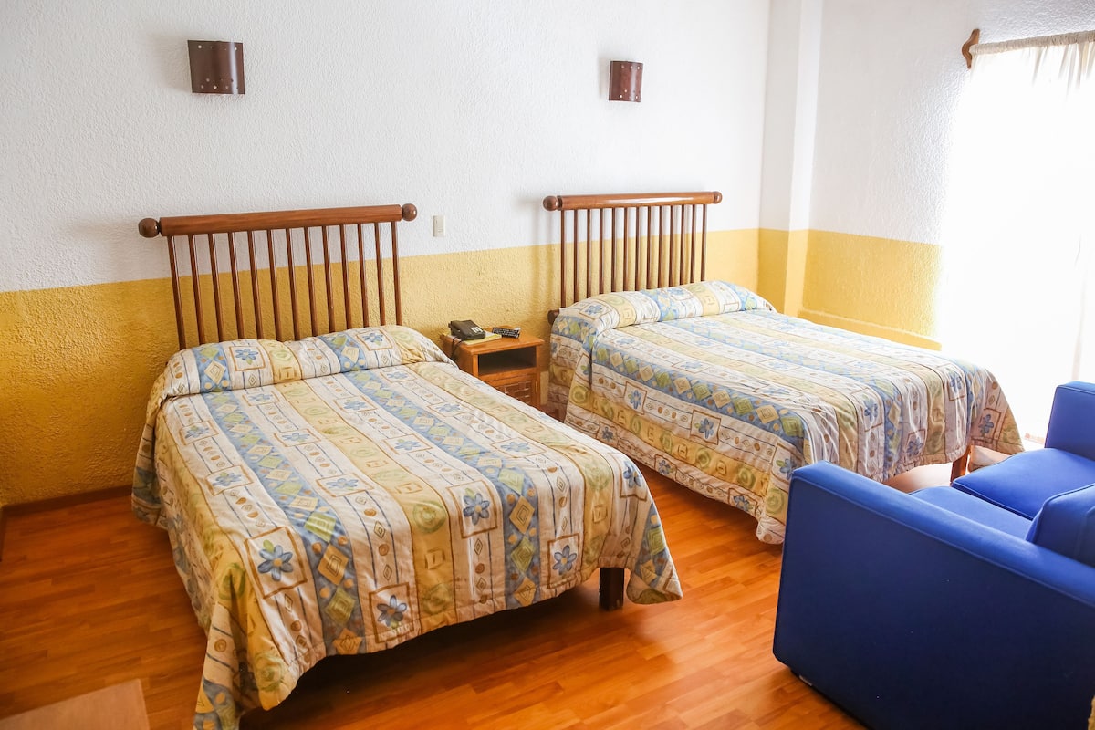 Ein Zimmer mit zwei Betten, Holzboden und einem blauen Stuhl.