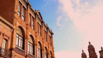 Ein historisches Gebäude mit Bogenfenstern und einem Balkon, gelegen in einem Platz mit Kopfsteinpflaster.